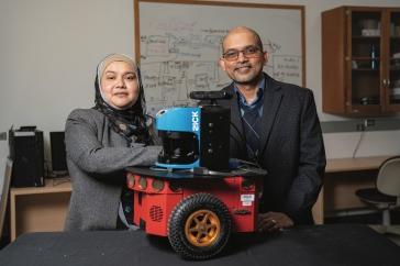 Two researchers stand in front of a red robot