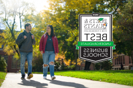 Two students walk along a path in fall alongside the Poets&Quants 2023 best business schools badge