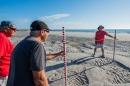 三个老人站在沙滩上，手里拿着测量棒来测量沙子的高度.